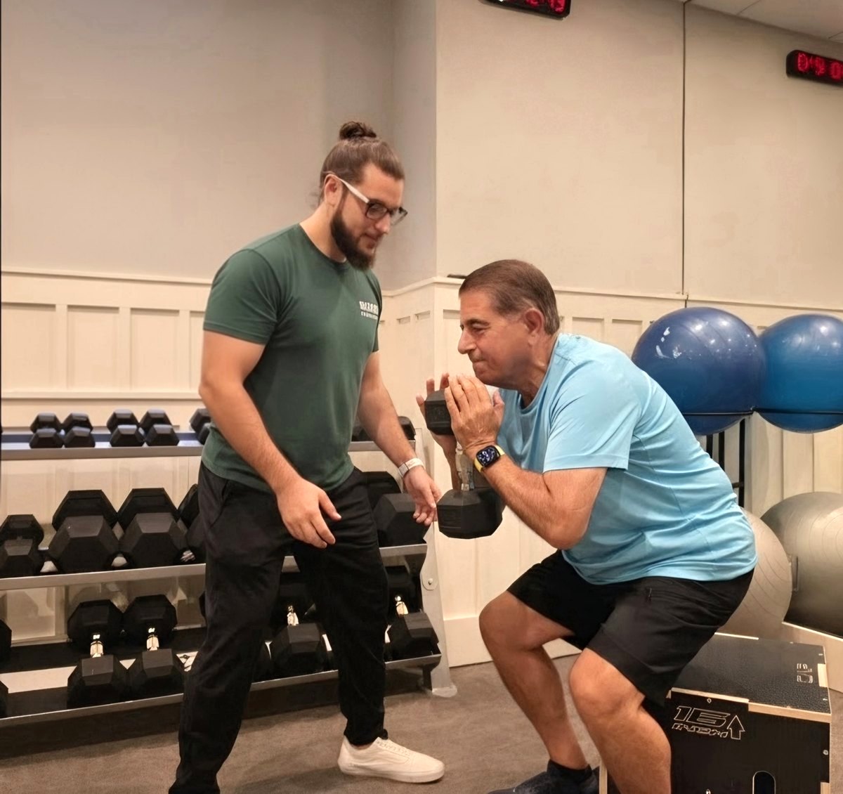 A physical therapist coaching an older adult through a supported squat with a dumbbell