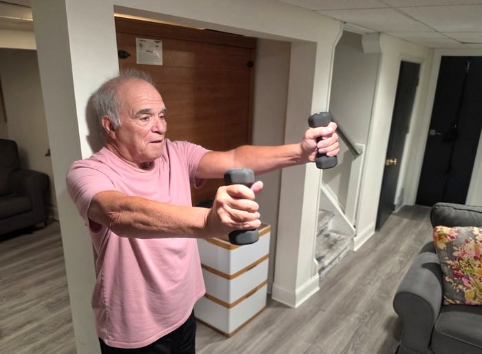 An older adult performing a front raise with dumbbells at home