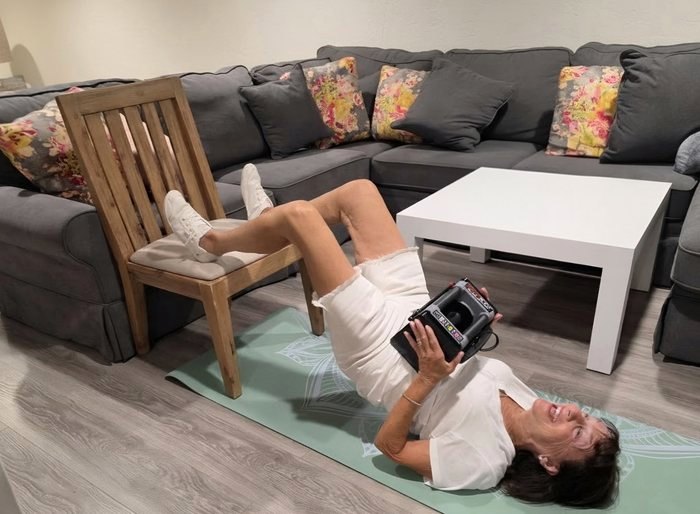 An older adult doing a supported floor exercise at home with a therapist