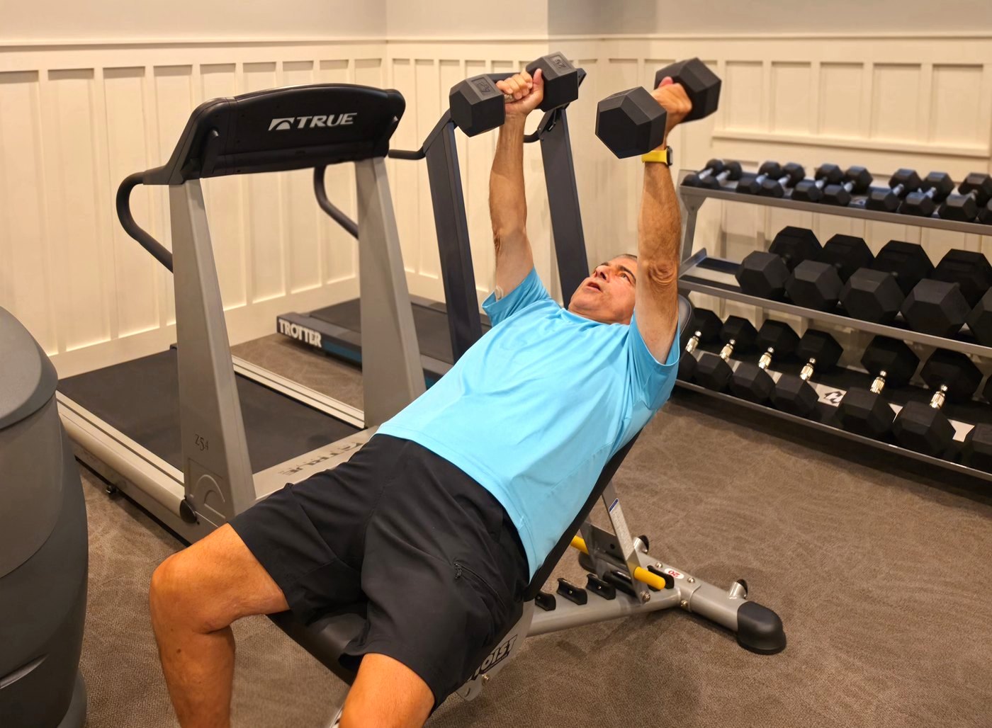 A man pressing dumbbells on an incline bench in a home gym